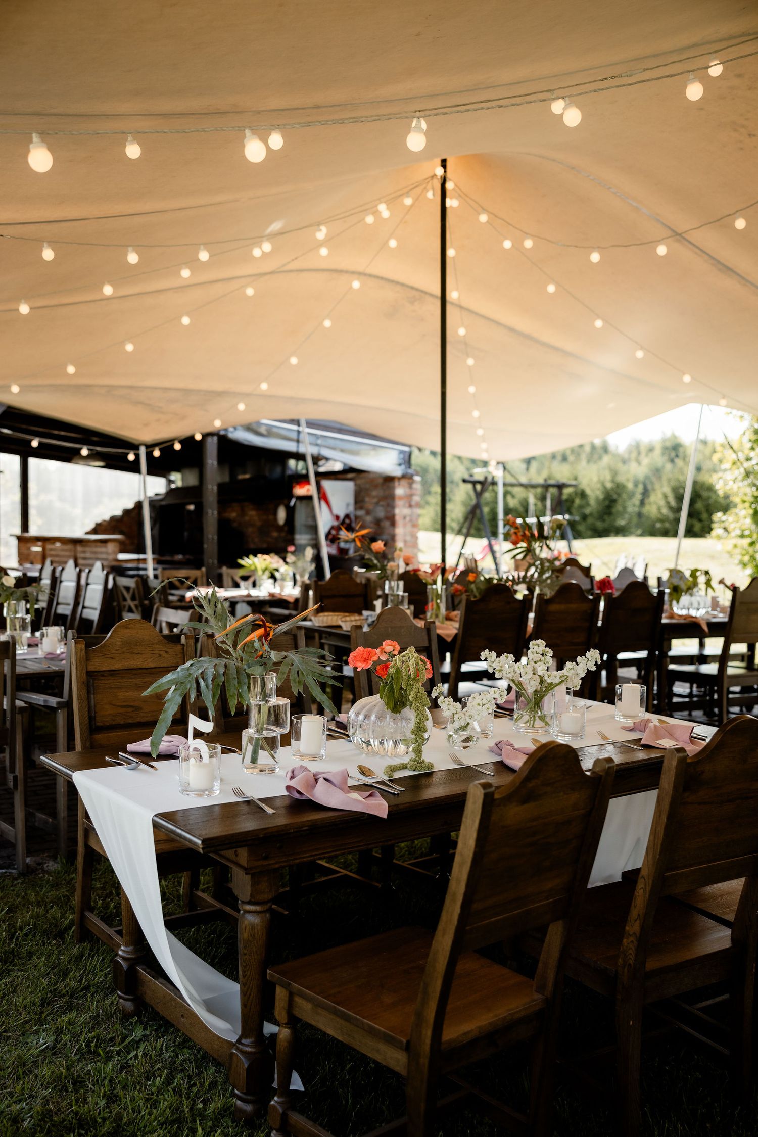 Rustic wedding reception tables set with white linens and string lights hanging overhead.