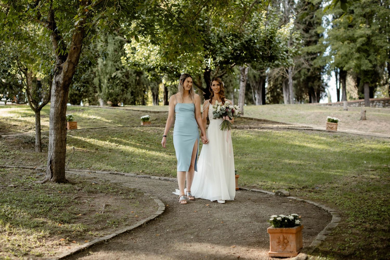 Two people walk together on a garden path during an elegant outdoor event on a sunny day.