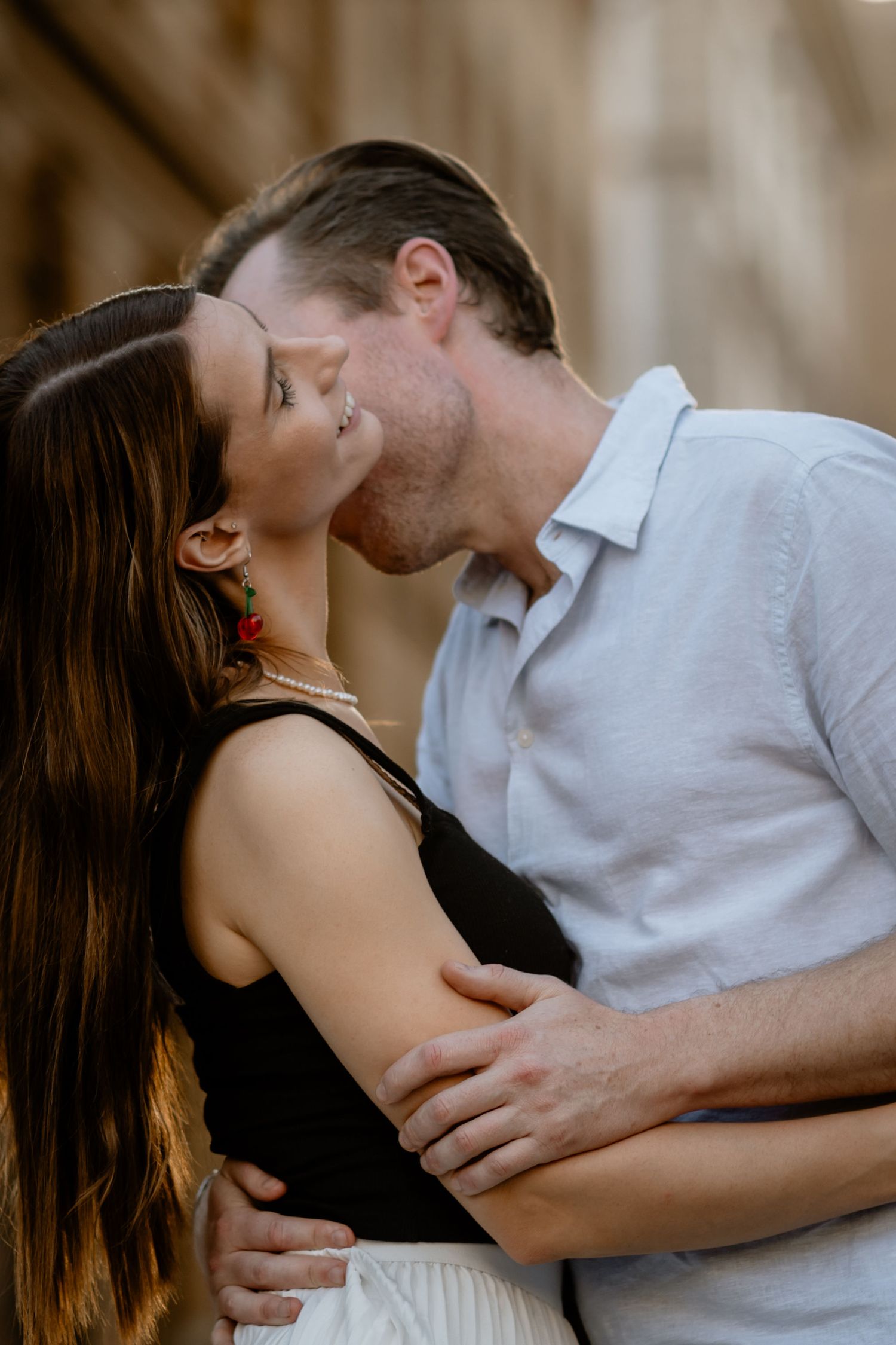 A couple shares a tender romantic kiss, with her in a black top and him in a light gray button-down shirt.