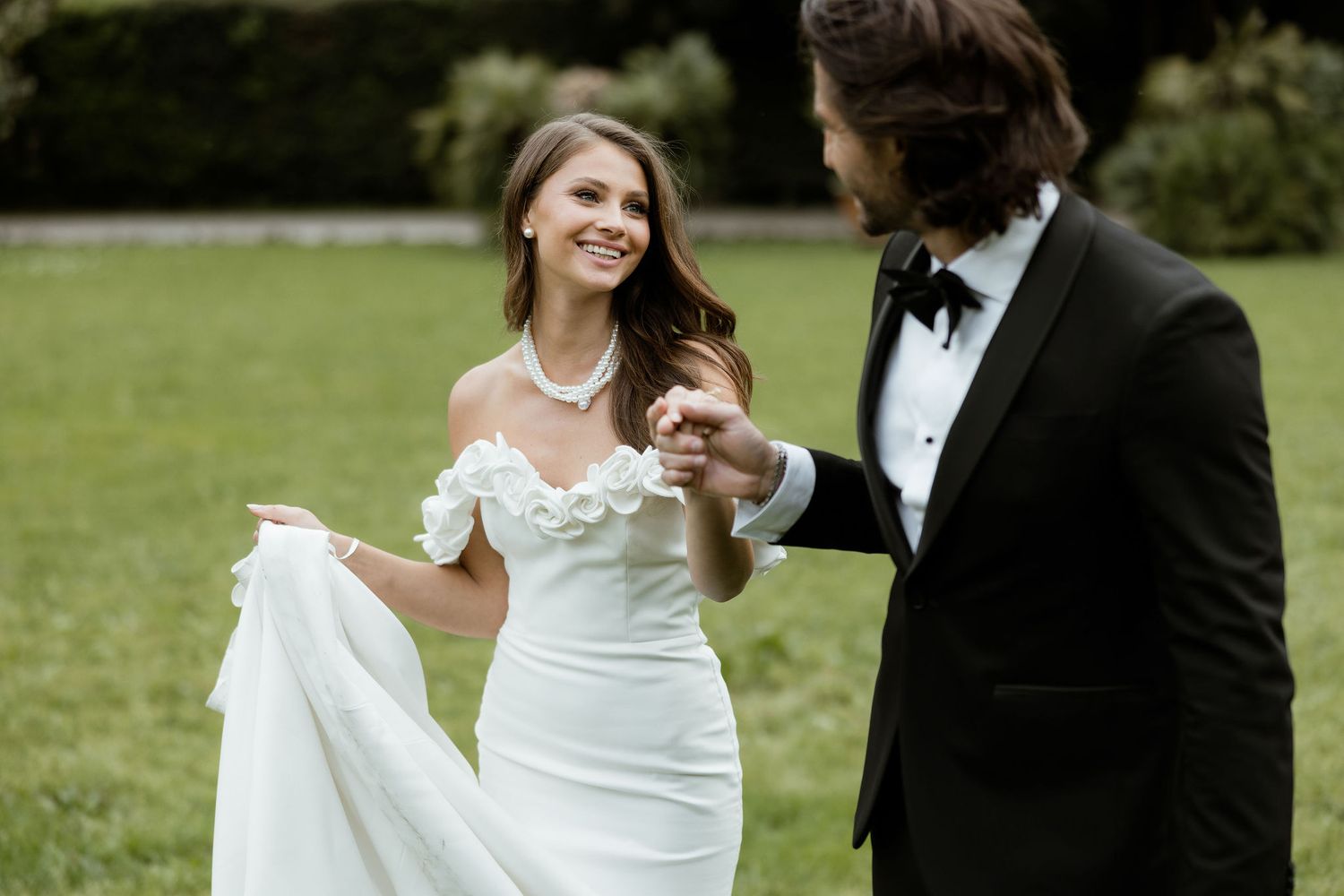 Newlywed couple share a joyful moment on a green lawn during their wedding day celebration.