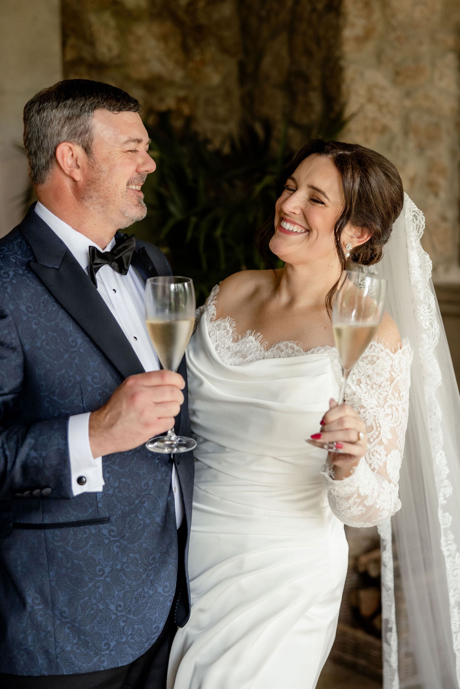 Newlywed couple sharing joyful laughter while holding champagne glasses at their elegant wedding celebration.