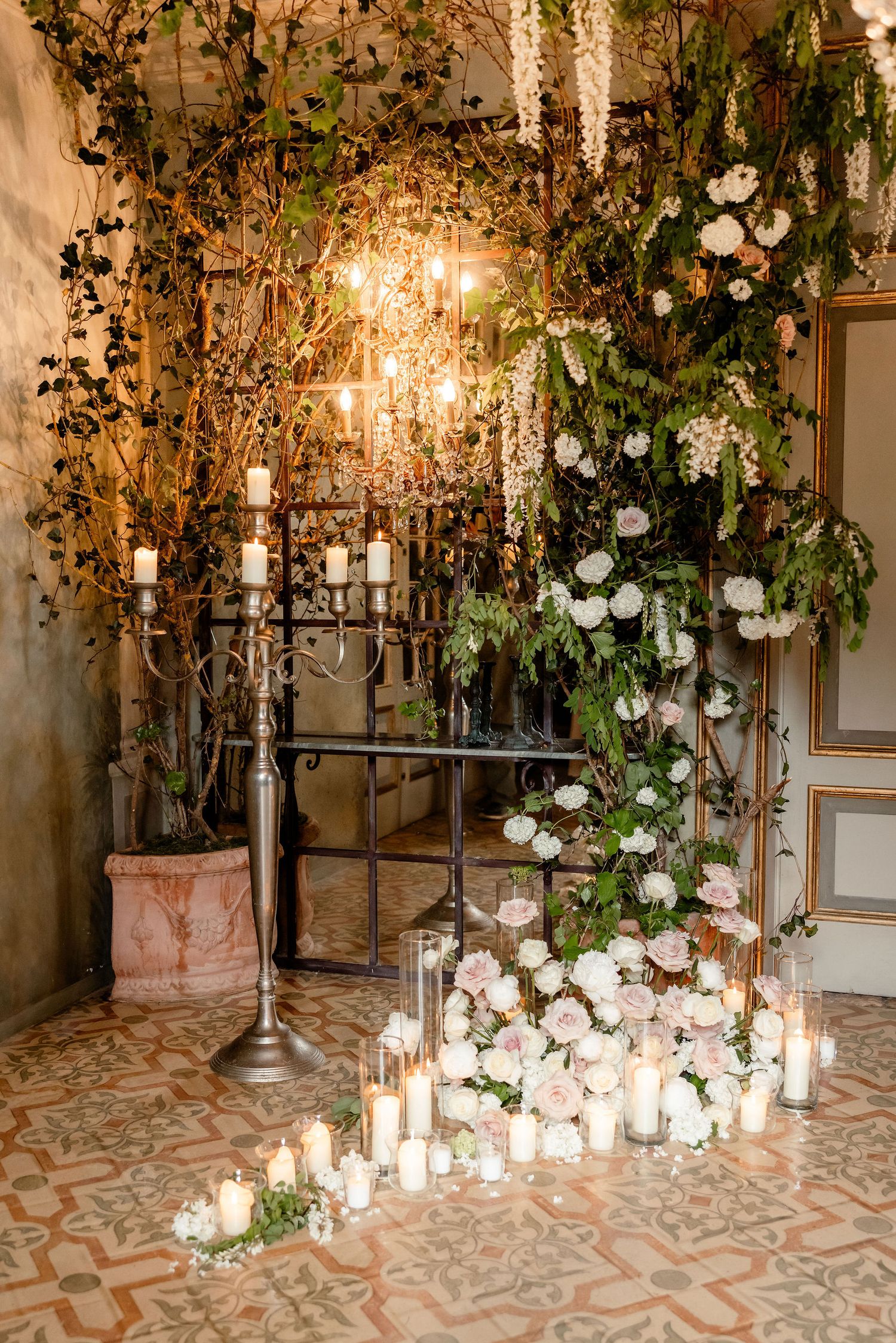 Romantic wedding decor with cascading white roses, candlelit lanterns, and rustic chandeliers in an elegant vintage setting.