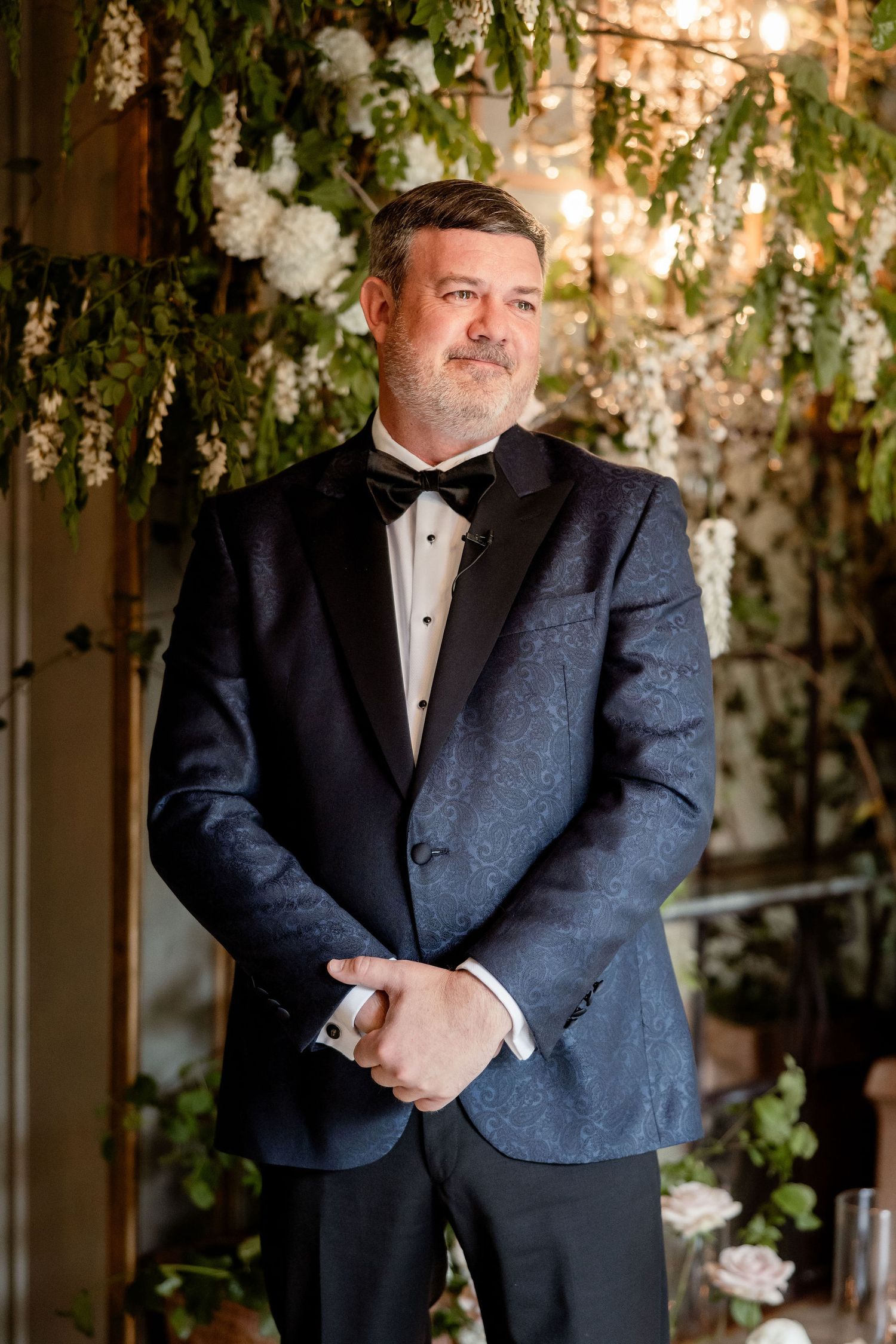 A person in formal attire poses in front of an elegant floral backdrop at a wedding venue.