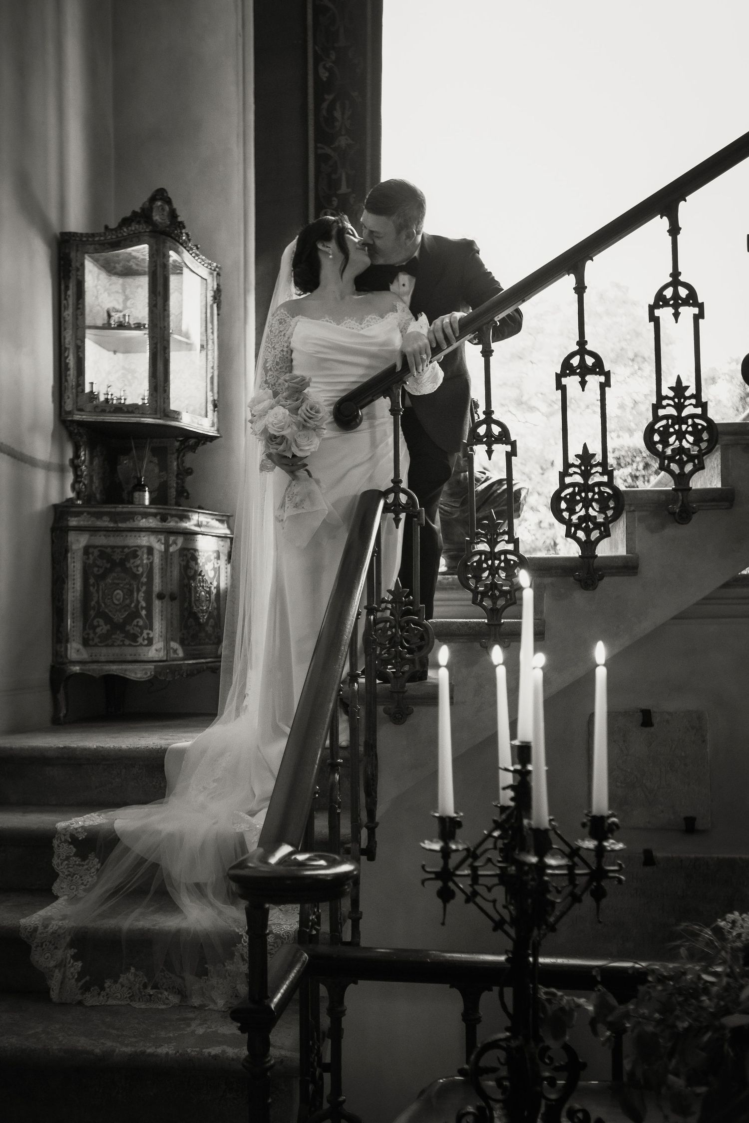 A romantic wedding scene on a staircase with ornate candelabras and lanterns in black and white.