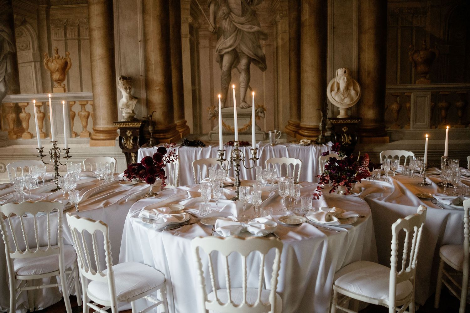 Elegant wedding reception table setting with white linens, candelabras and antique decor in an ornate historic venue.
