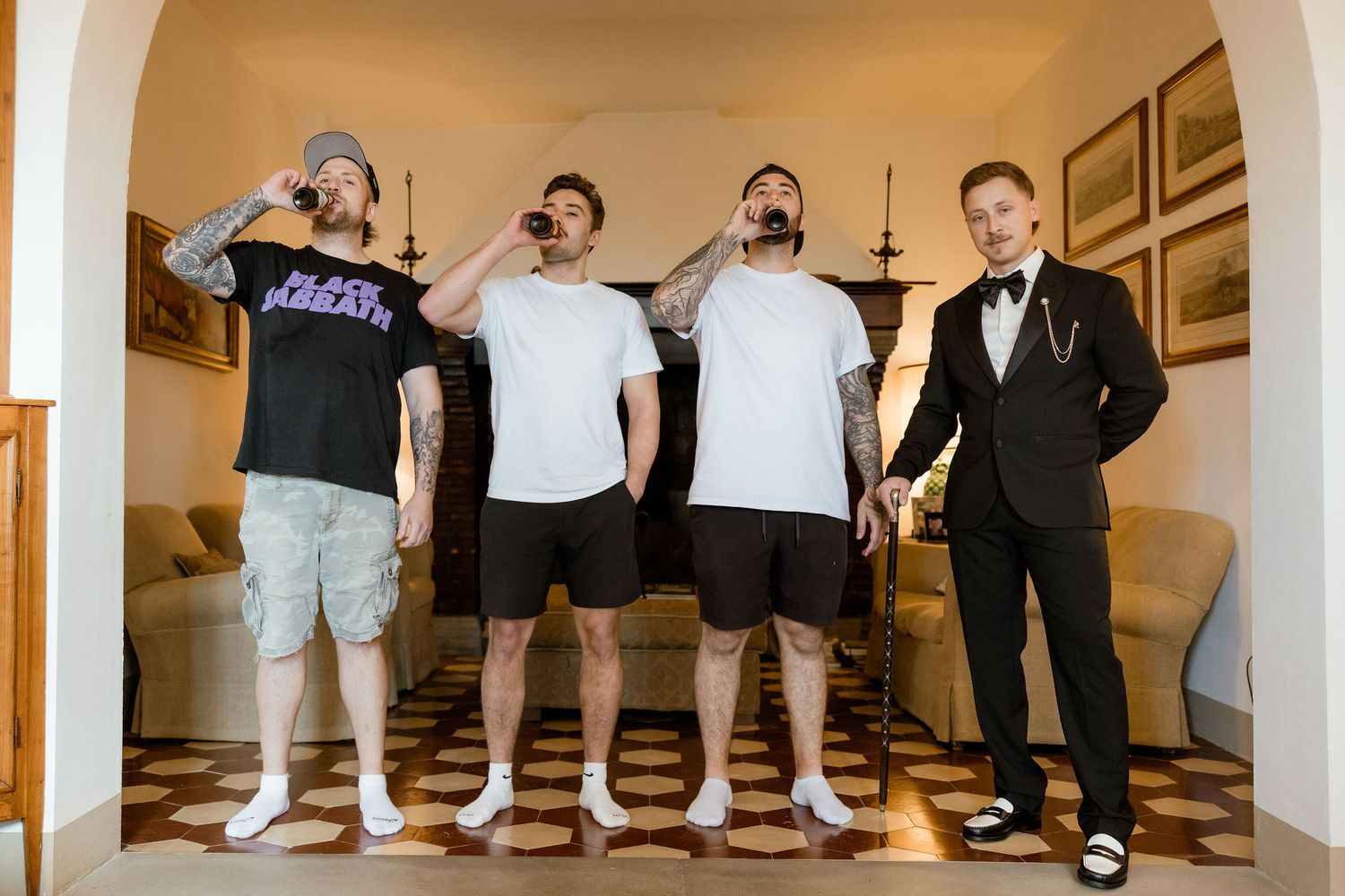 Four people standing together in casual and formal attire inside a room with beige walls and framed artwork.