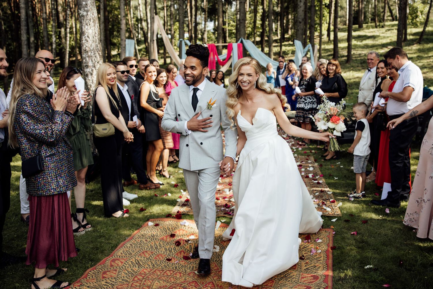 Couple walks down outdoor aisle while wedding guests celebrate.