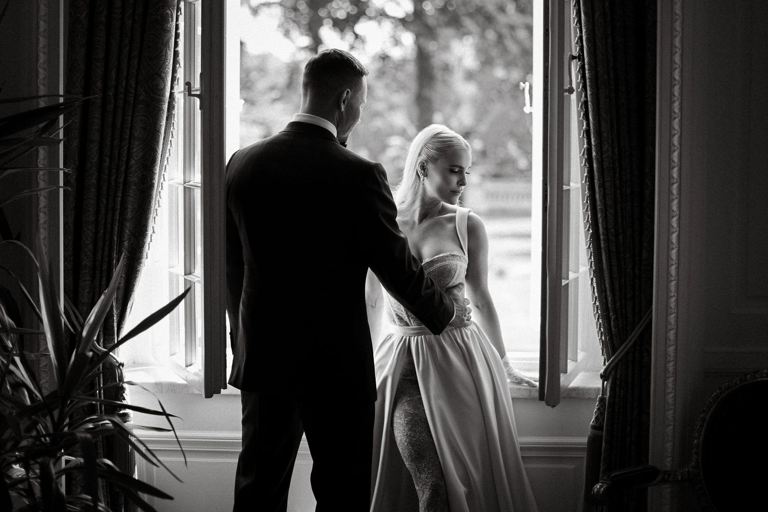 Elegant black and white portrait of couple by window with dramatic lighting.