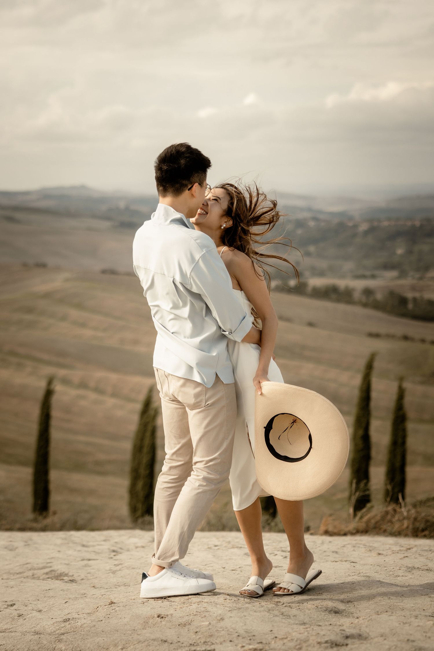 A couple shares an intimate moment against a backdrop of rolling hills and cypress trees in Tuscany.