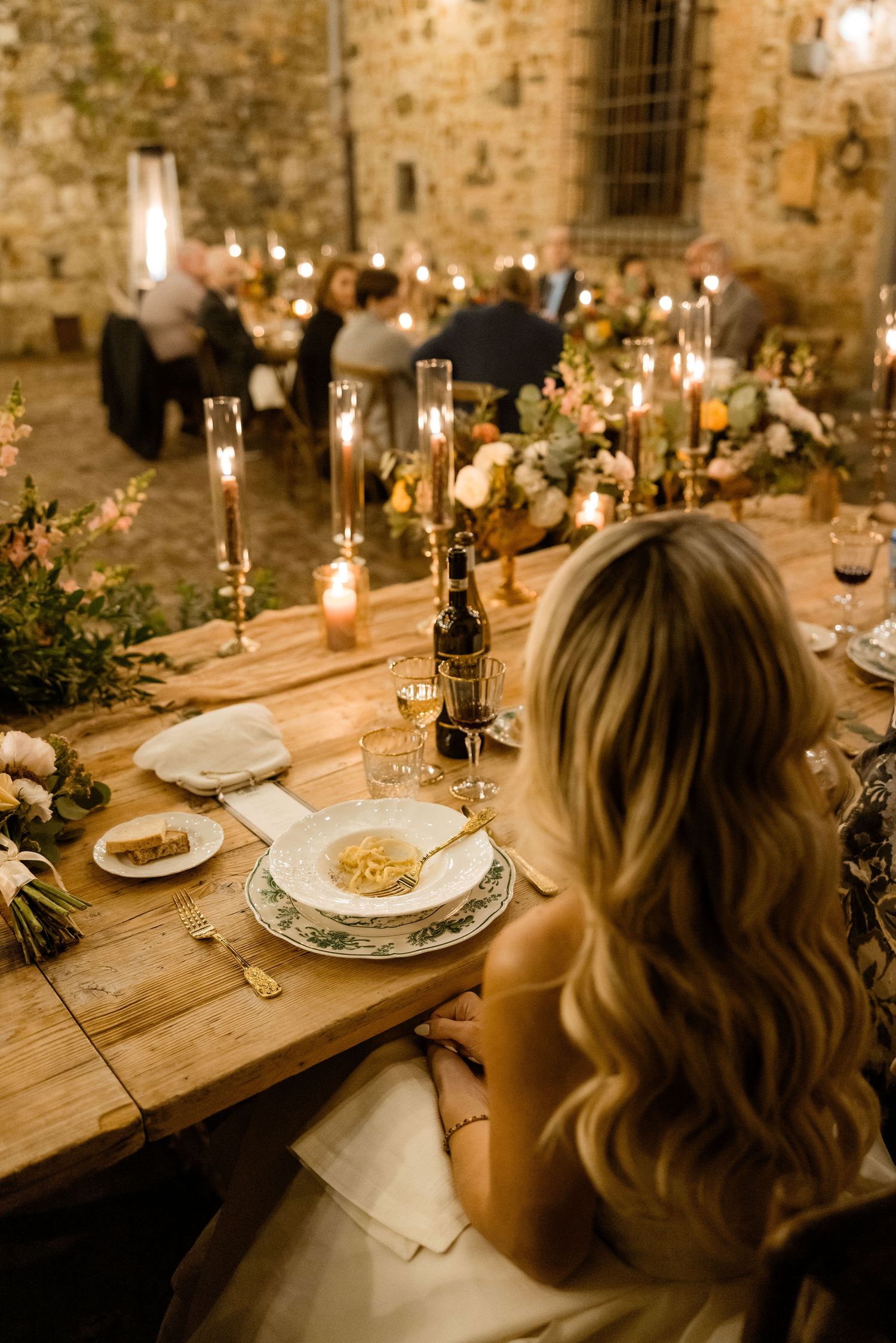 Rustic wooden dining table set with elegant candles and place settings in a stone-walled venue for an intimate dinner.