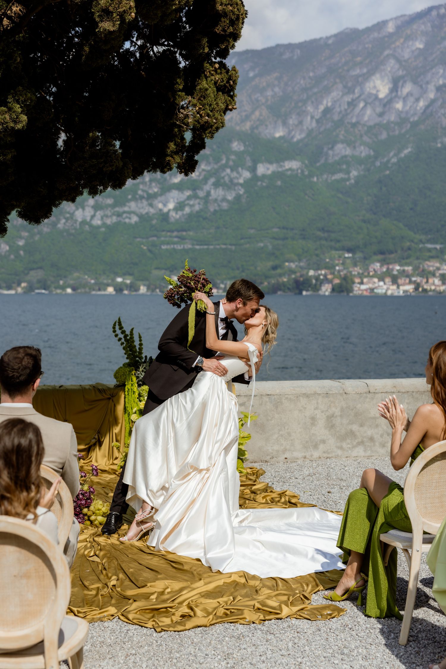 Bride and groom share first kiss at outdoor Lake Como wedding ceremony with mountain backdrop.
