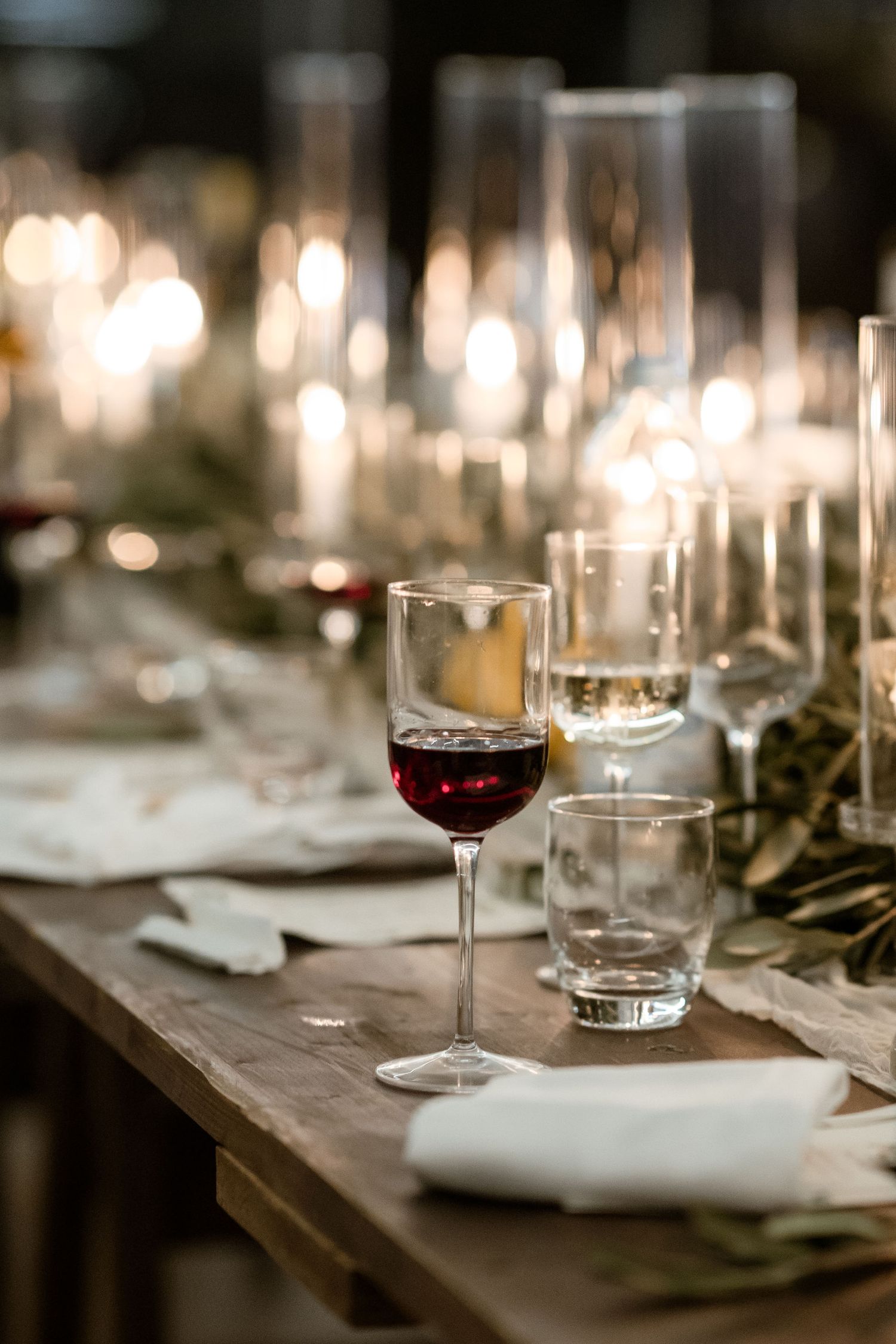 Wine glasses and place settings arranged on a rustic wooden table with soft bokeh lighting in the background.