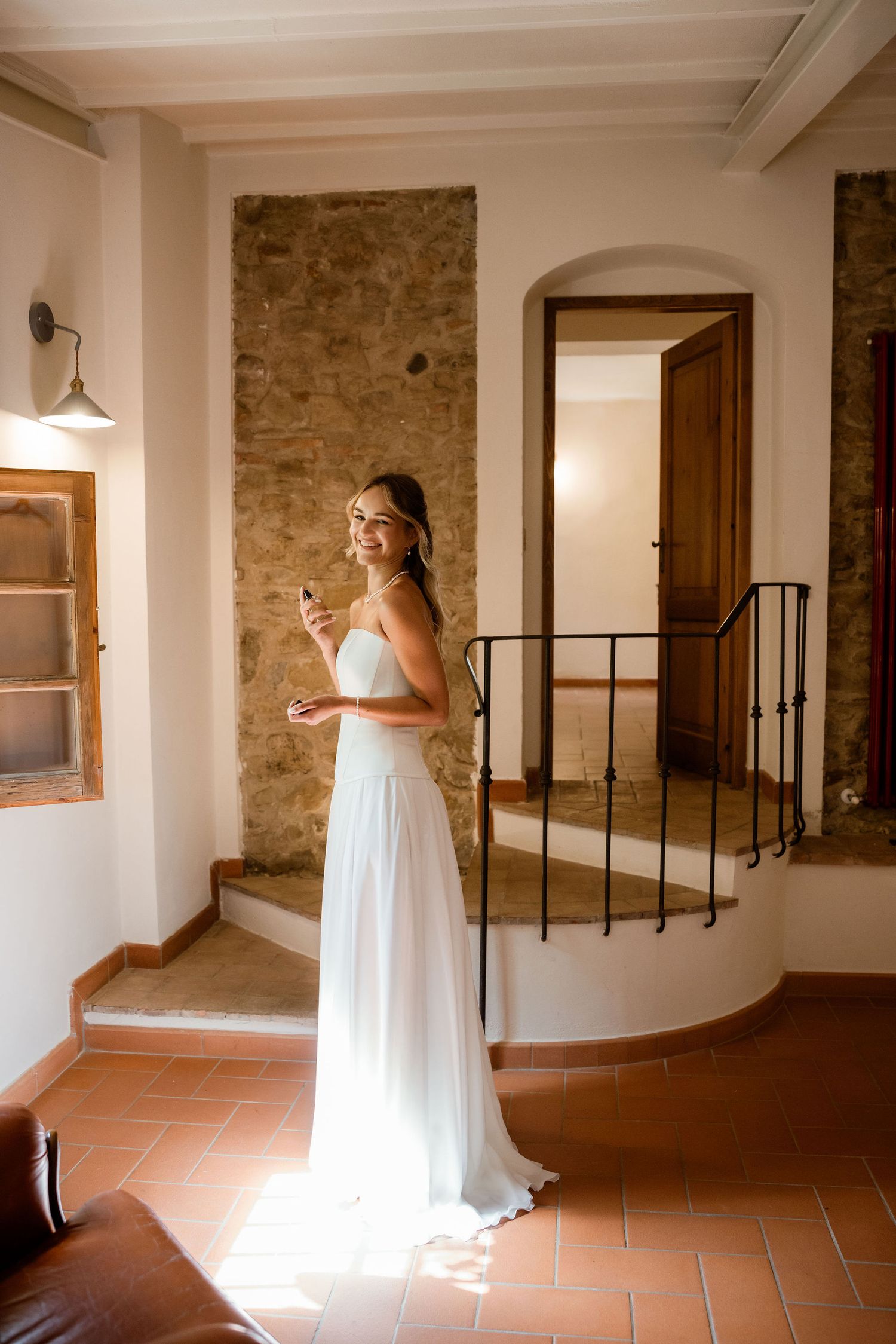 A figure in a flowing white dress walks through a rustic interior hallway with stone walls and terracotta floors.