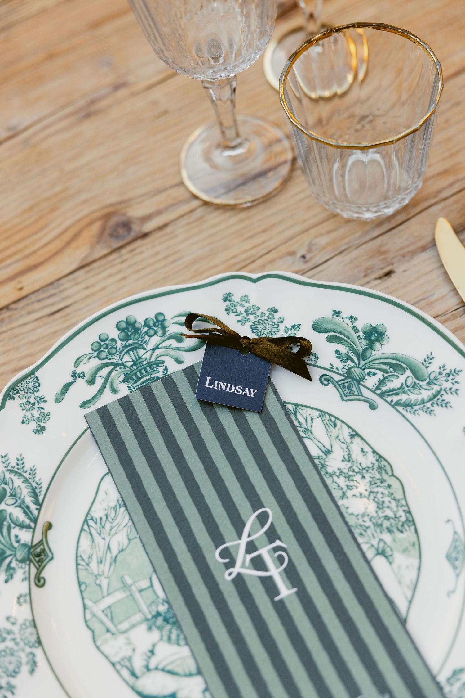 A set of elegant place settings with green and white patterned plates and wine glasses on a wooden table.