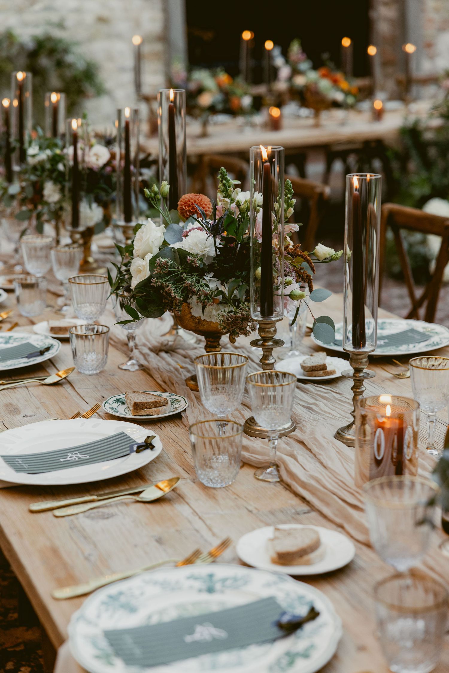 Elegant wedding reception table setting with black candles, white plates, and natural greenery decorations.