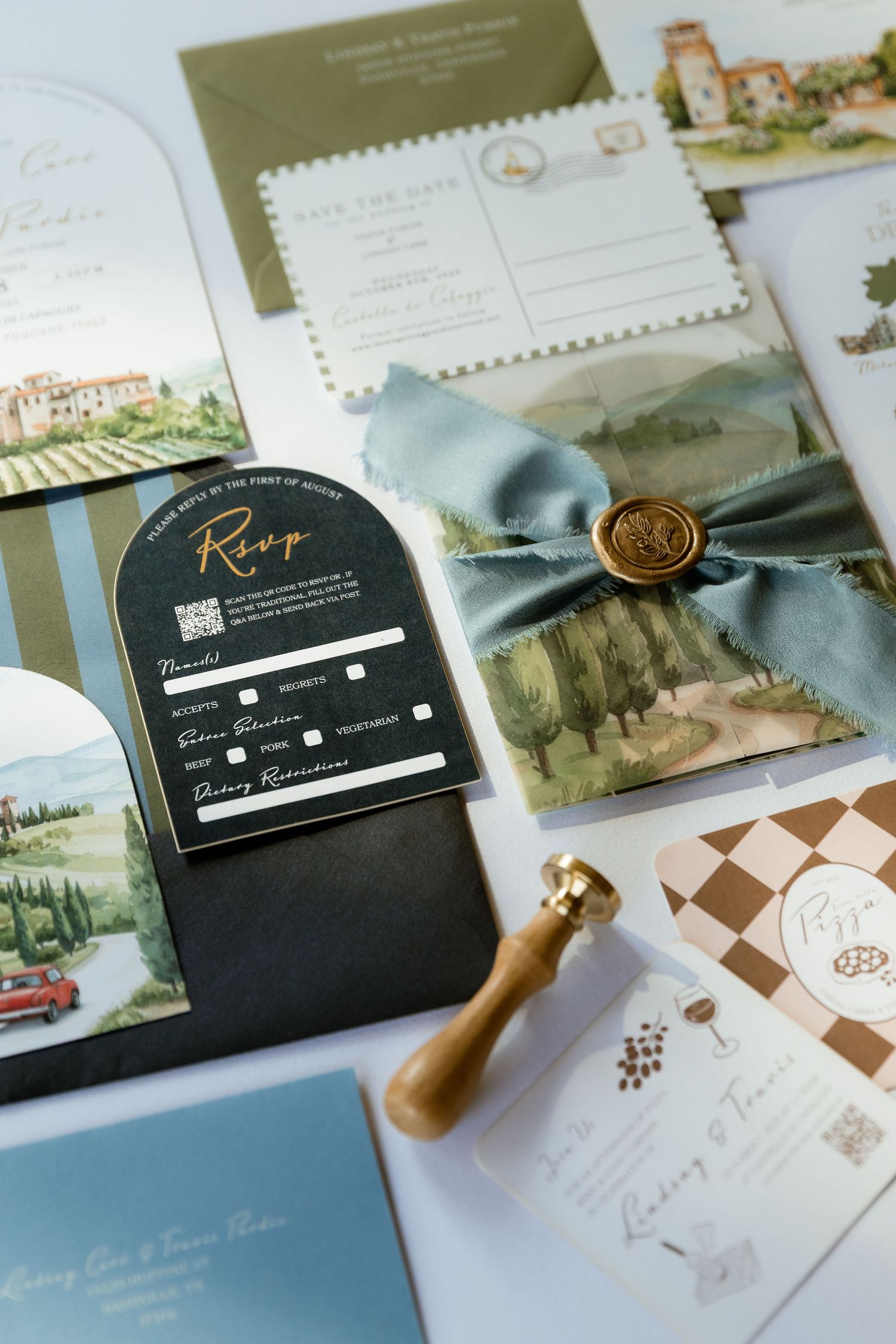 Elegant wedding invitation suite with watercolor illustrations, black wax seals, and postage stamps displayed on a light surface.