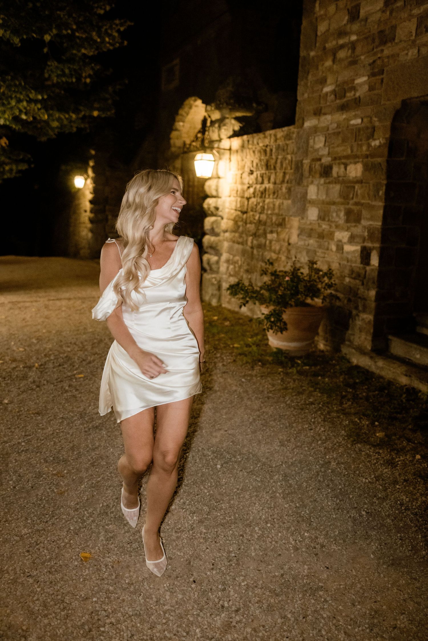 A series of nighttime photos showing someone dancing and twirling in a white dress against stone walls and lanterns.