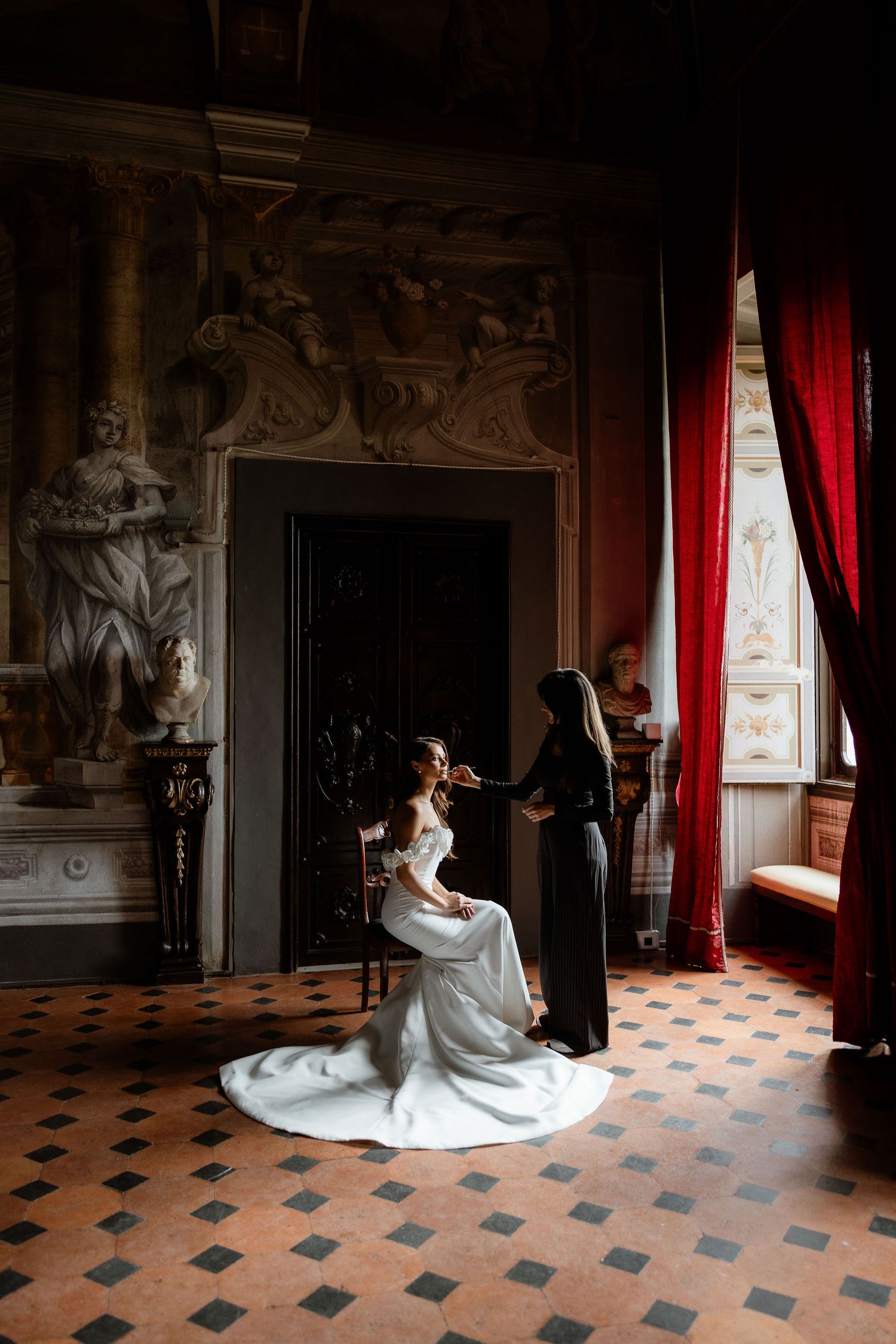 Elegant scene in ornate room with tiled floor, red curtains and dramatic lighting capturing an intimate wedding moment.