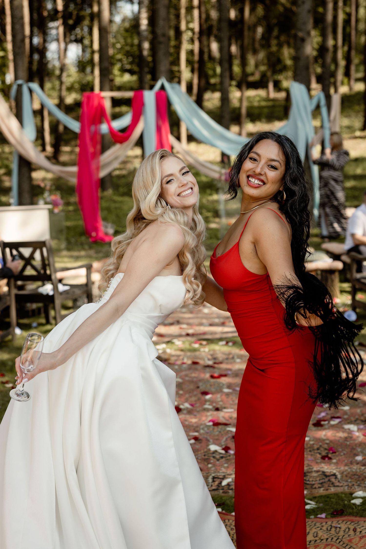 Two attendees pose playfully at an outdoor wedding with red and blue decorative drapes.