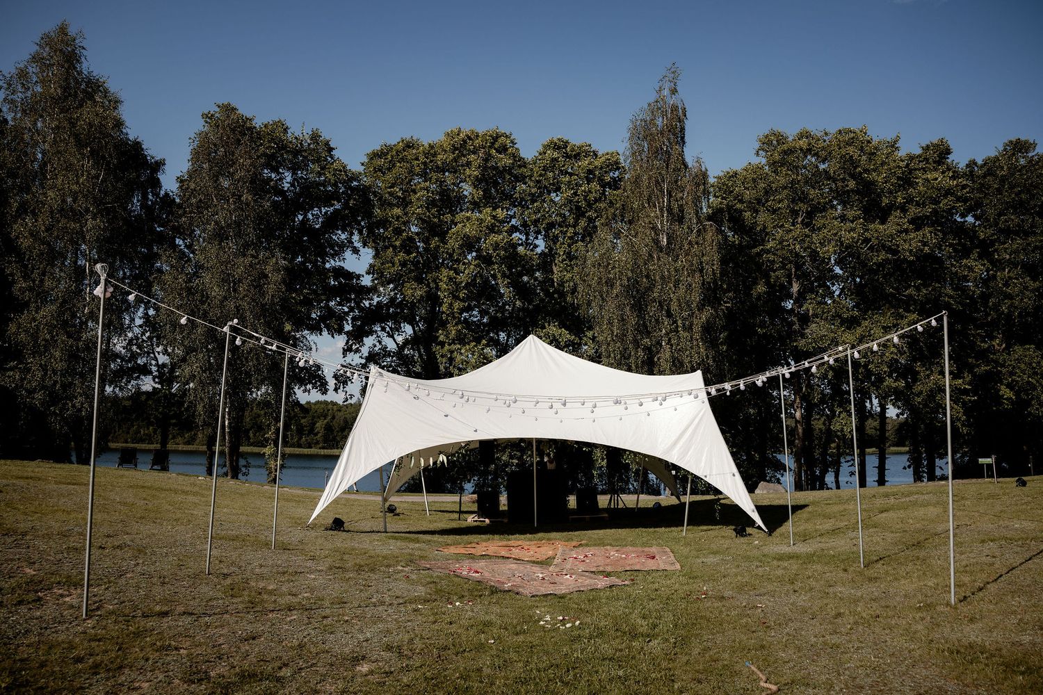 White stretch tent set up in grassy field with tall trees in background.