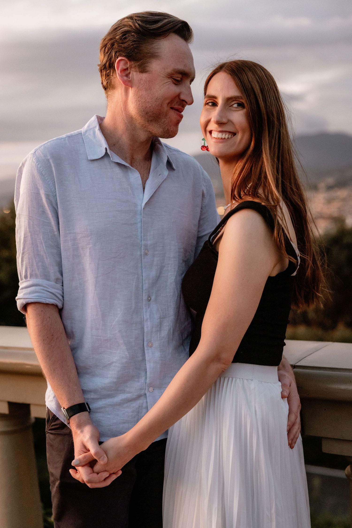 A romantic couple shares an intimate moment at sunset on a balcony overlooking a mountainous landscape.