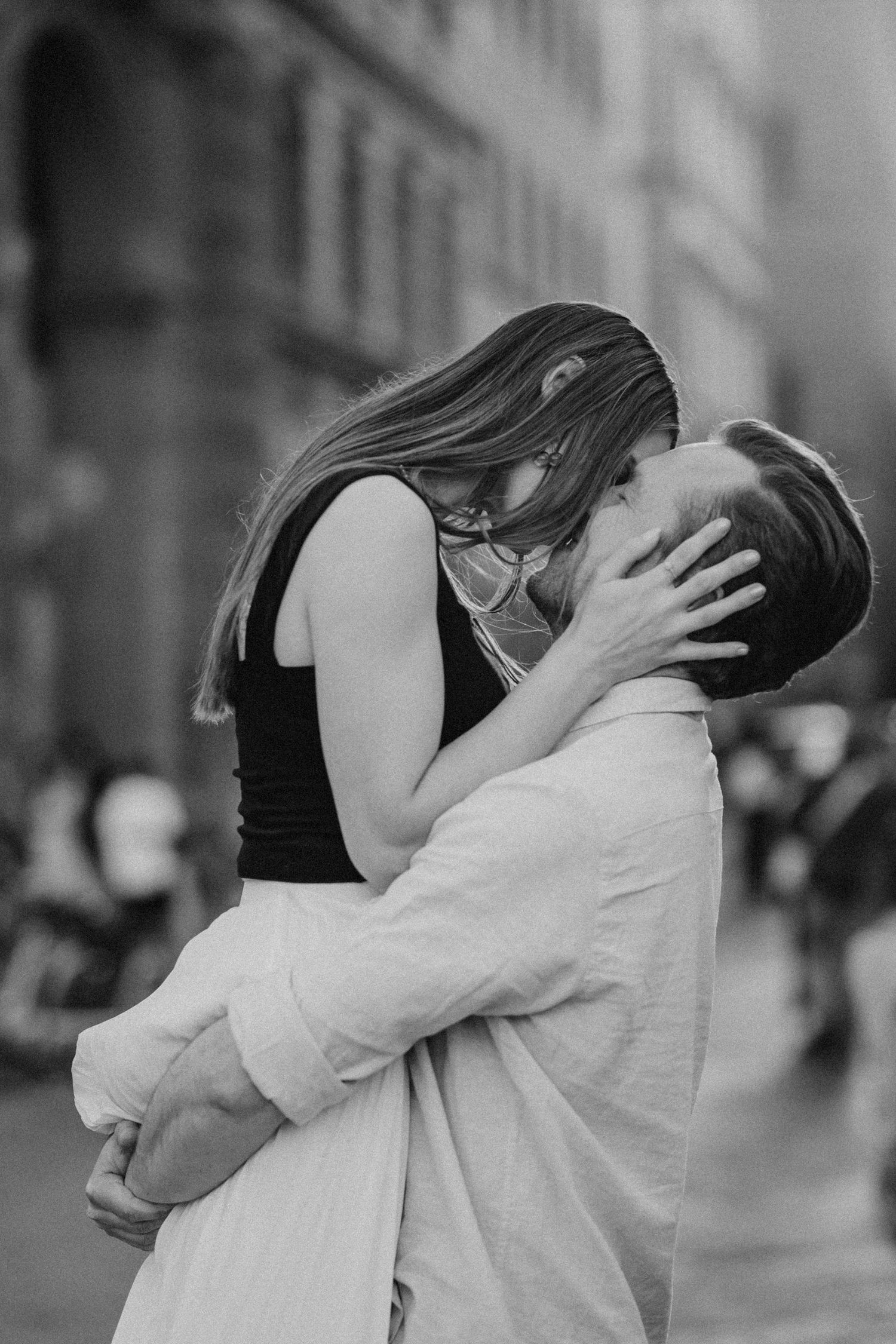 A romantic black and white photograph captures a couple sharing a passionate kiss on a city street.