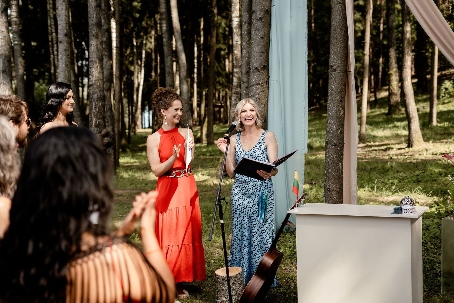 Attendees participate in an outdoor wedding ceremony under flowing red and blue fabric decorations.