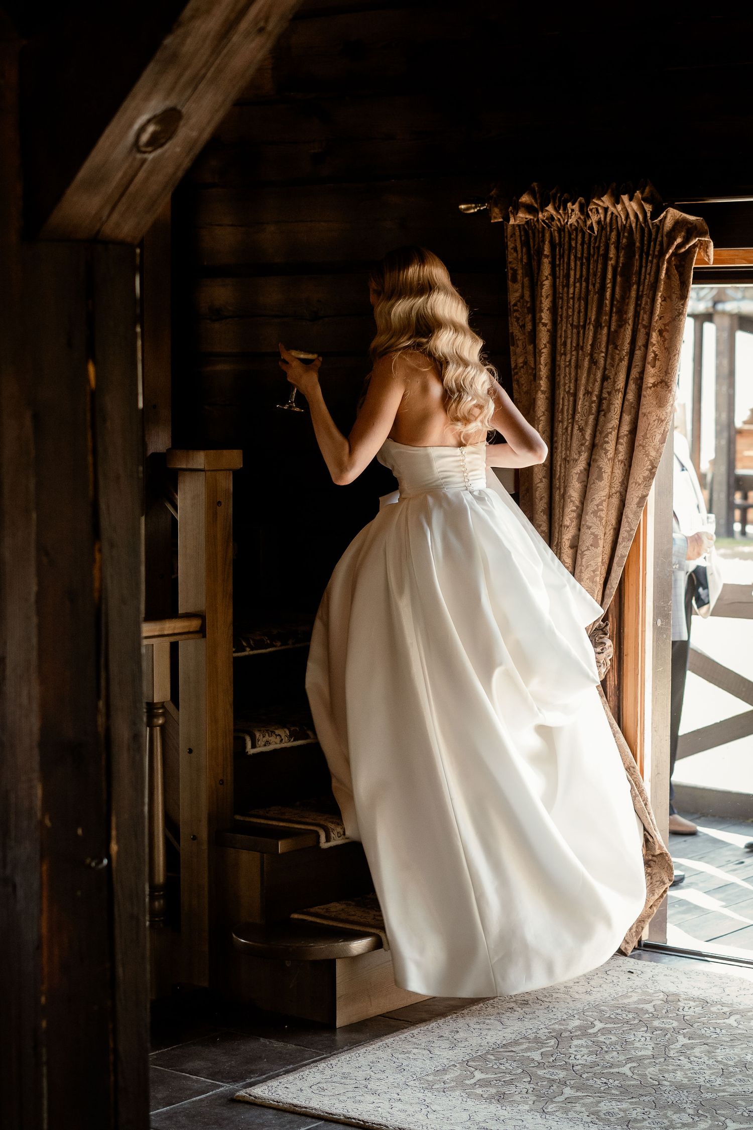 Back view of bride in elegant white dress ascending wooden stairs.