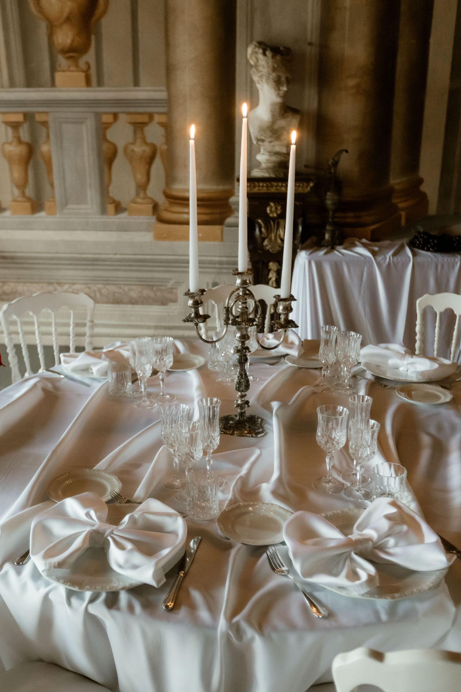 Elegant wedding table setting with white linens, crystal glassware and silver candelabra in an ornate historic venue.