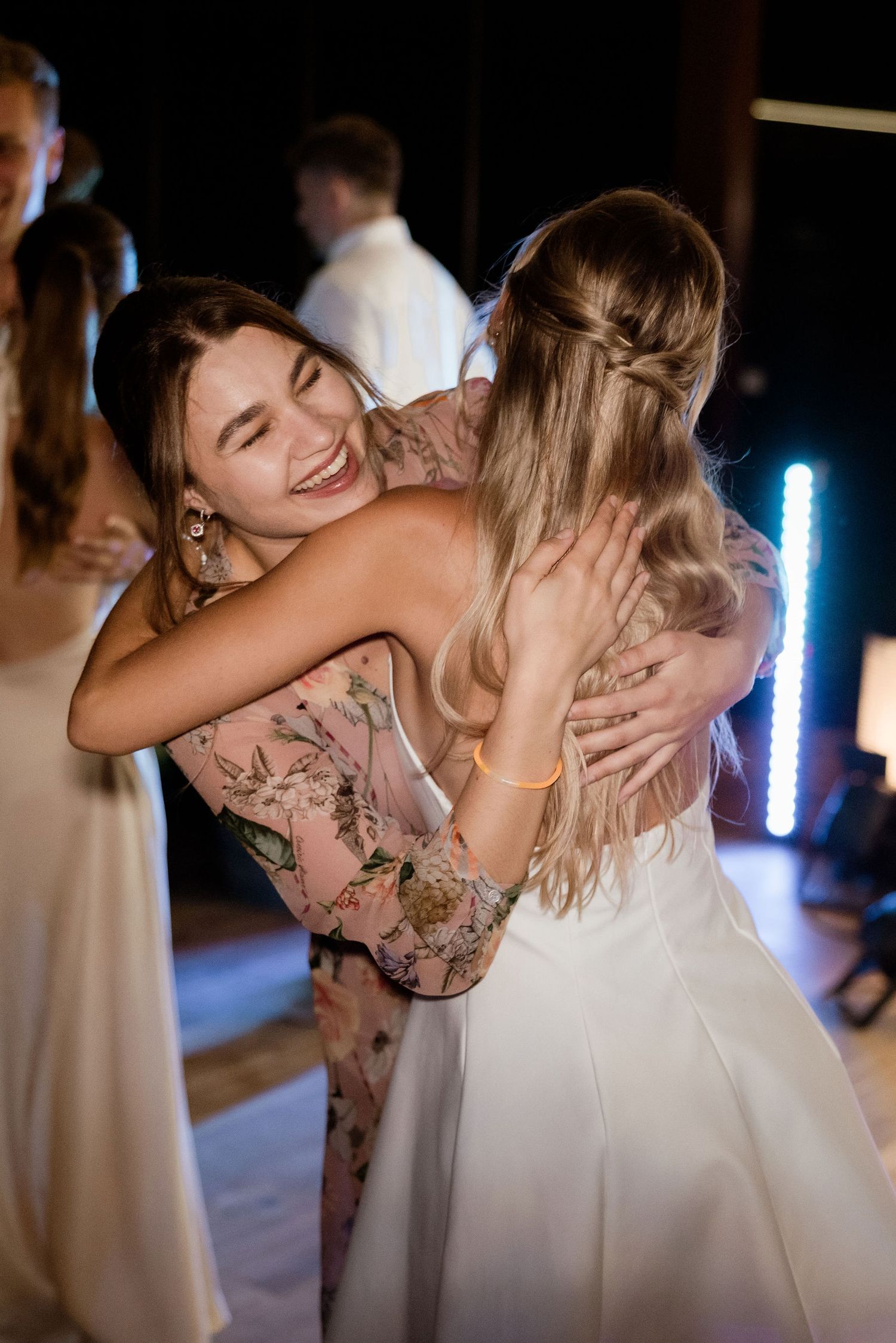 Two people share an emotional embrace on a dance floor at a wedding reception with blue lighting in the background.