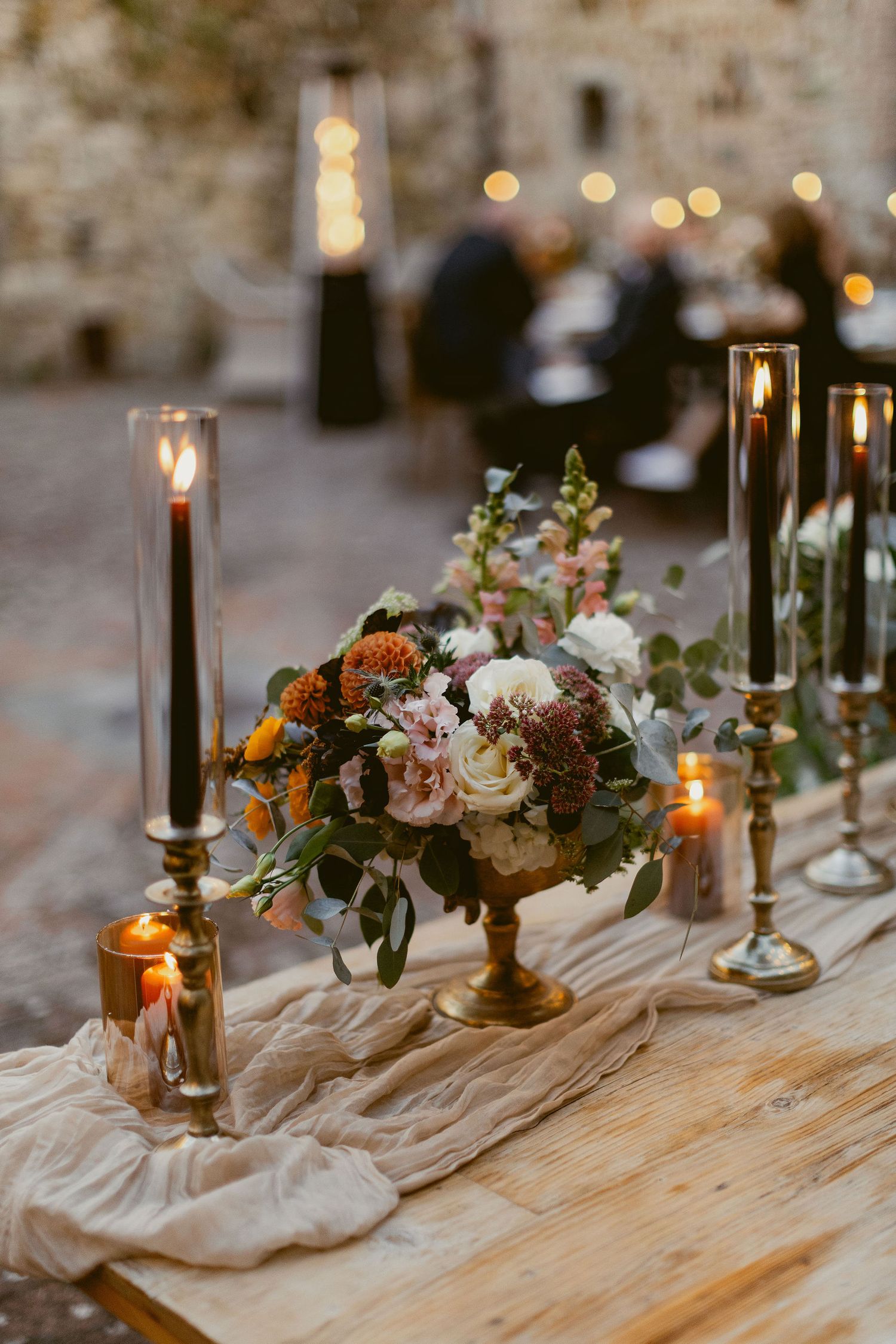 Rustic wedding table decor with candlesticks and floral arrangements on a wooden table with flowing fabric runner.