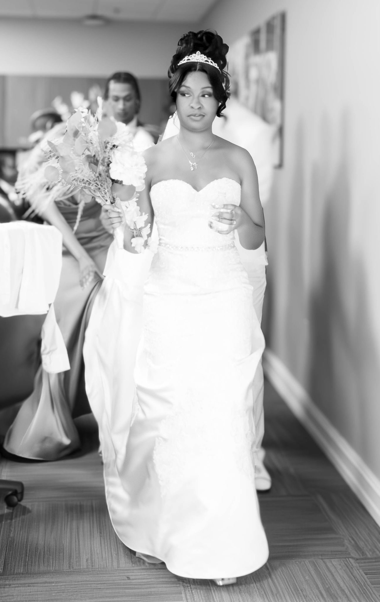 A radiant bride walking down a hallway carrying a white bouquet.