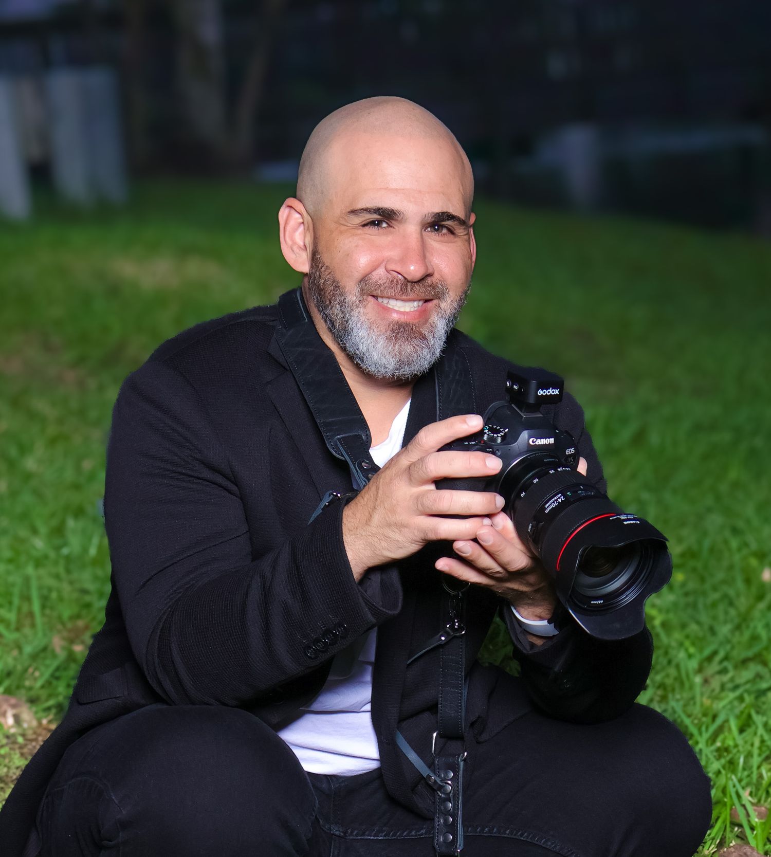 Professional photographer holding a DSLR camera while sitting outdoors on grass.