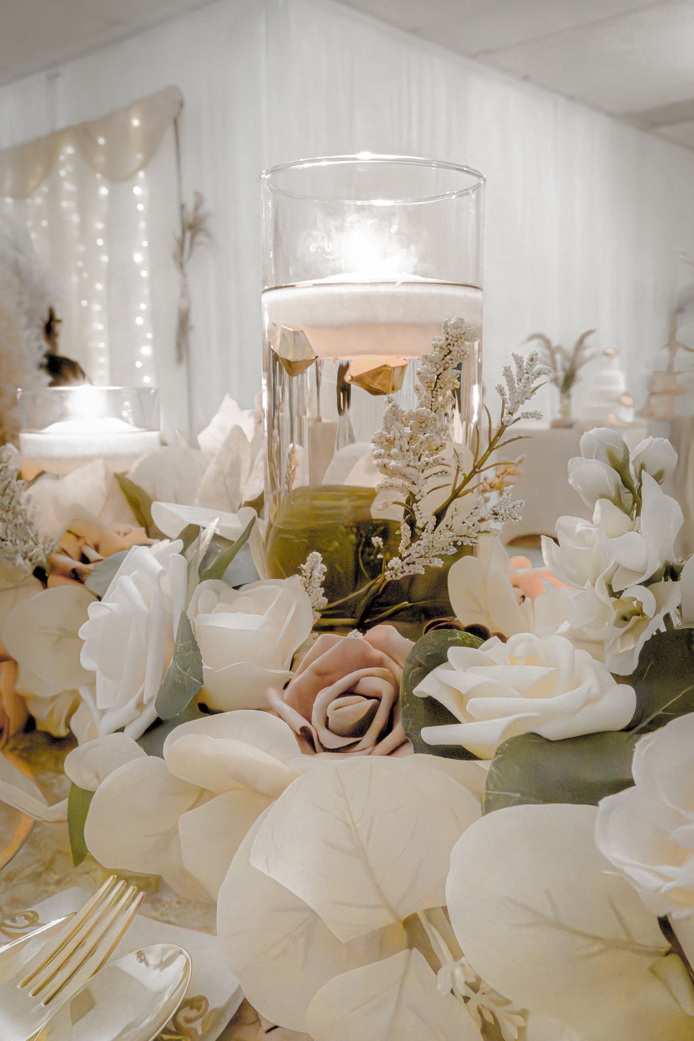 Wedding centerpiece with white roses and floating candles in glass vessels.