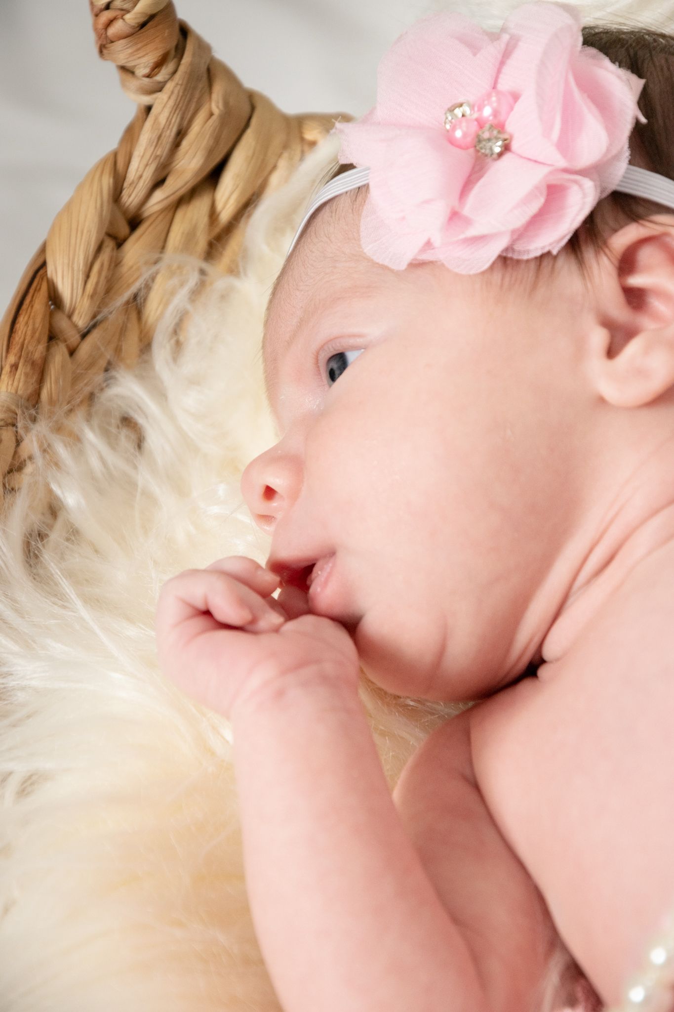 Sweet portrait of a baby wearing a pink flower headband lying on soft fabric.