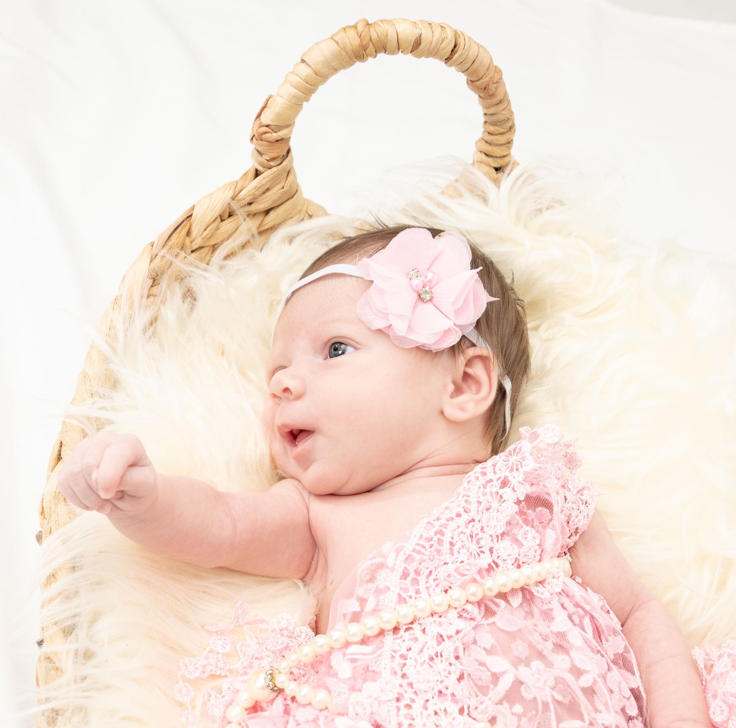Baby wearing pink floral dress and headband lying on cream colored textured blanket.