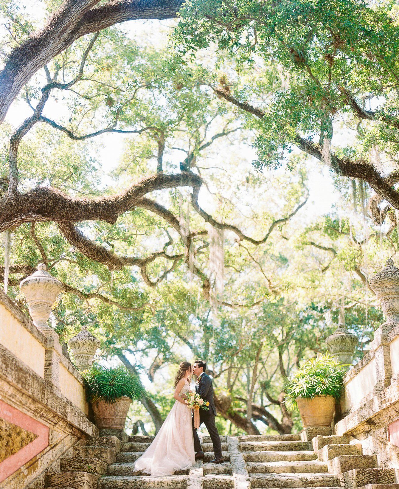 Elegant wedding scene on grand stone staircase surrounded by majestic oak trees.