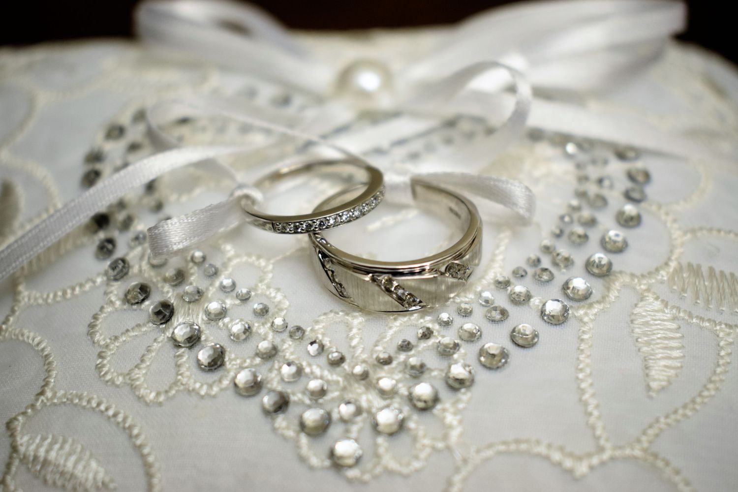 Wedding rings displayed on delicate white lace fabric with crystal embellishments.