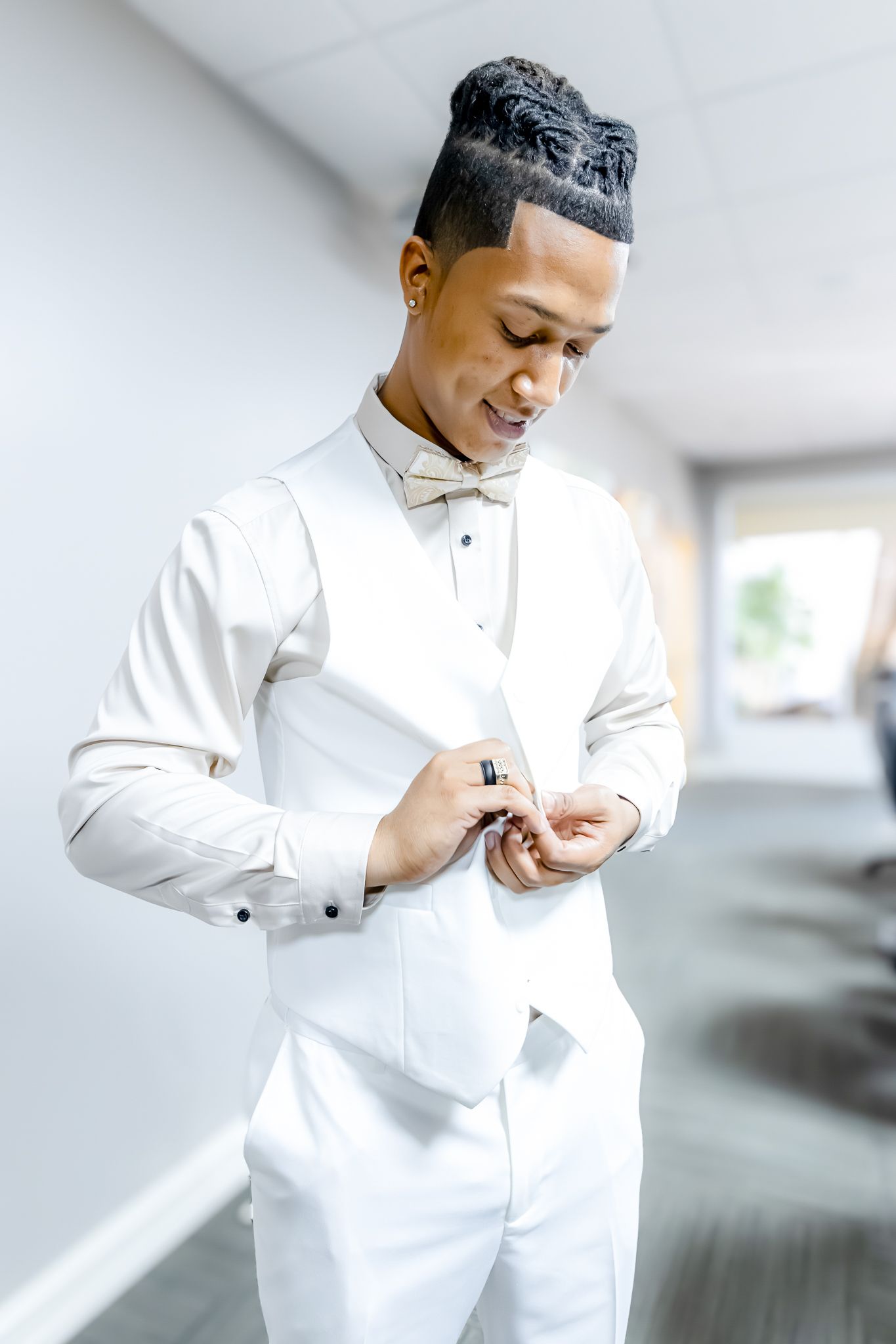 Groom adjusts buttons on his elegant white wedding suit while standing in a hallway.