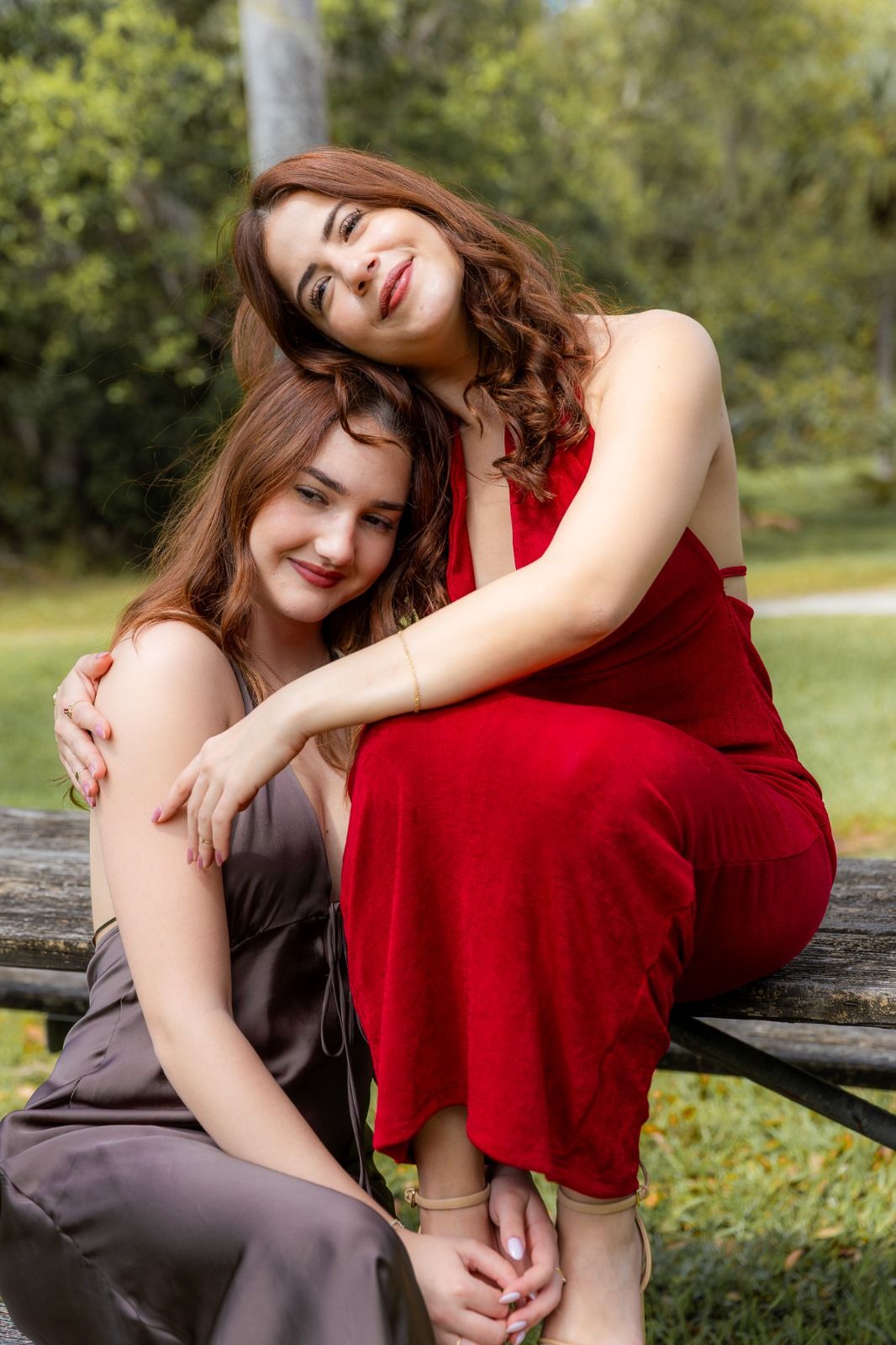 Two friends embracing outdoors wearing red and brown dresses.
