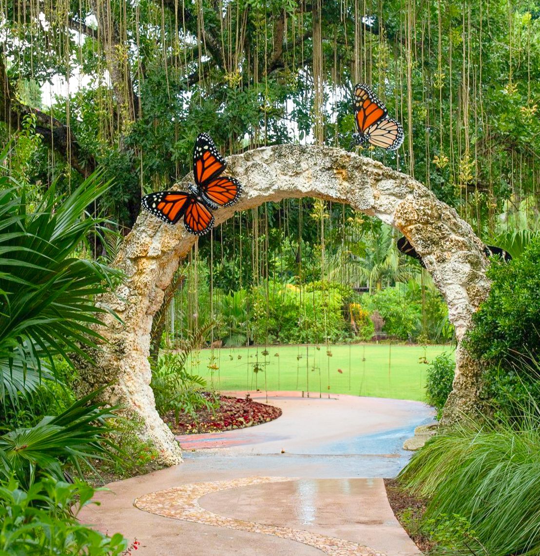 Garden pathway under a decorative stone arch adorned with monarch butterflies and hanging vines.