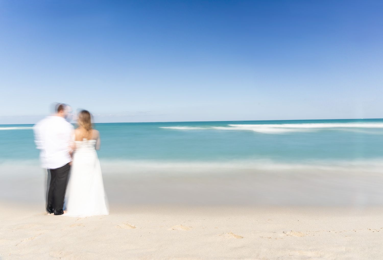 A couple walking along a pristine white sandy beach with turquoise ocean waters and clear blue sky in the background.
