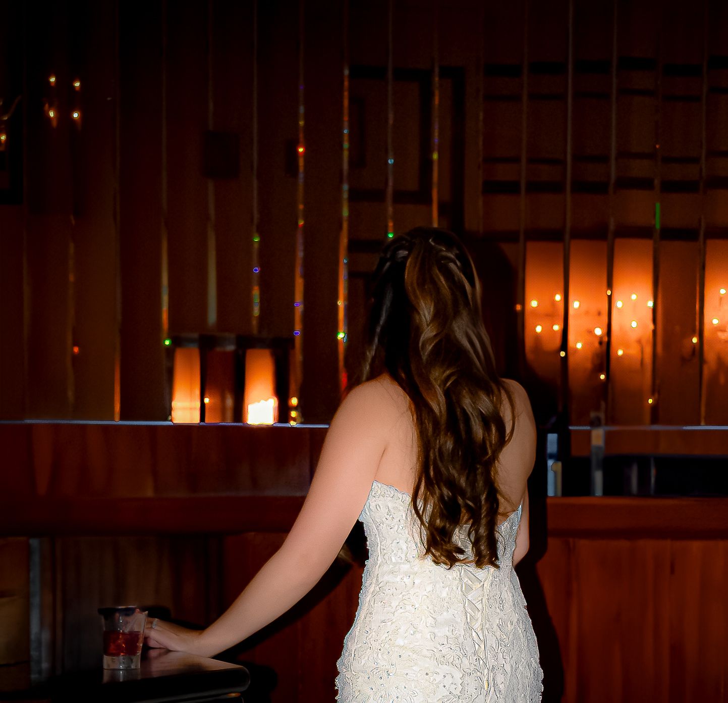 Silhouette of bride in white dress against warm glow of candlelit background.