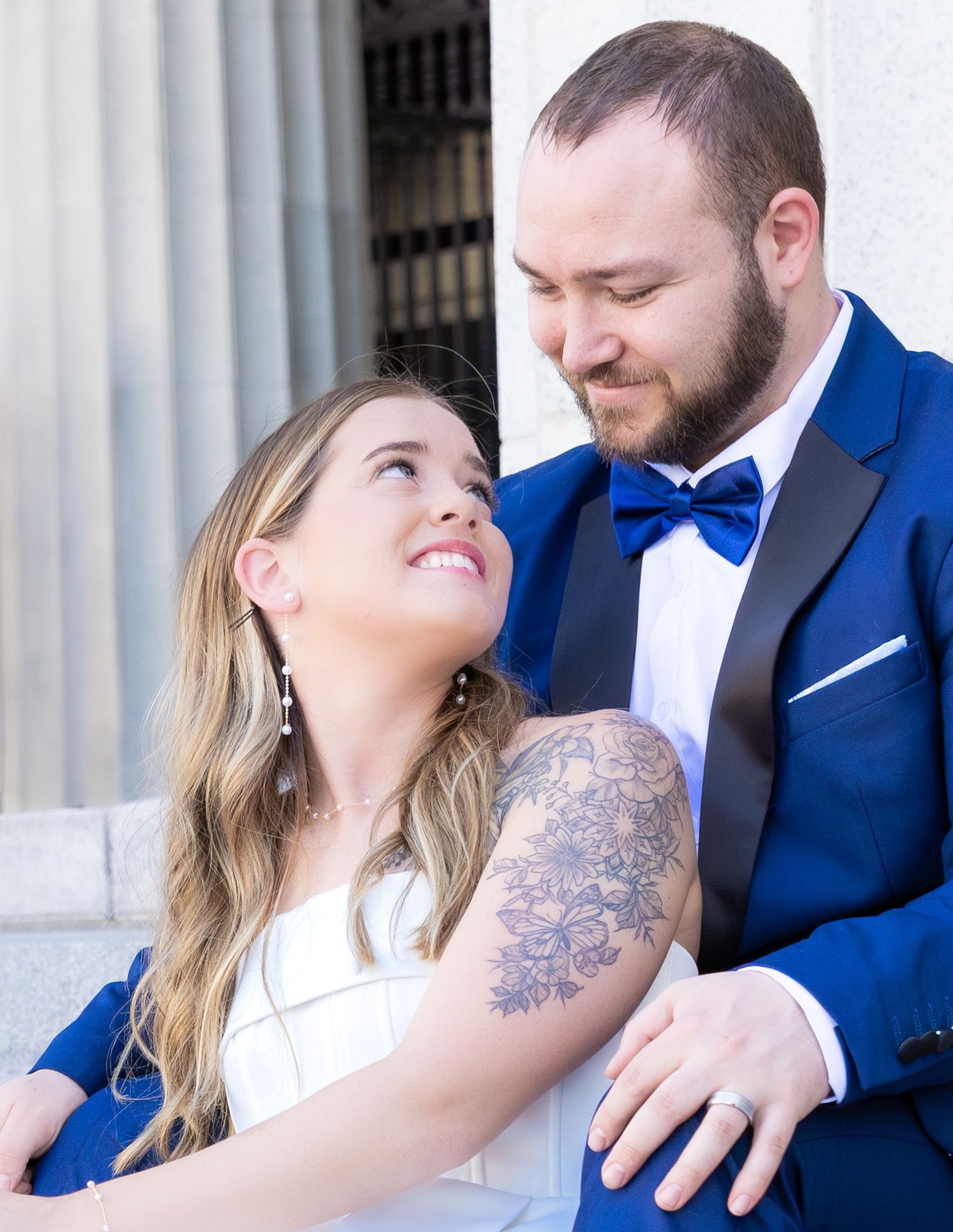 Intimate portrait of couple with visible floral arm tattoo against white columns.