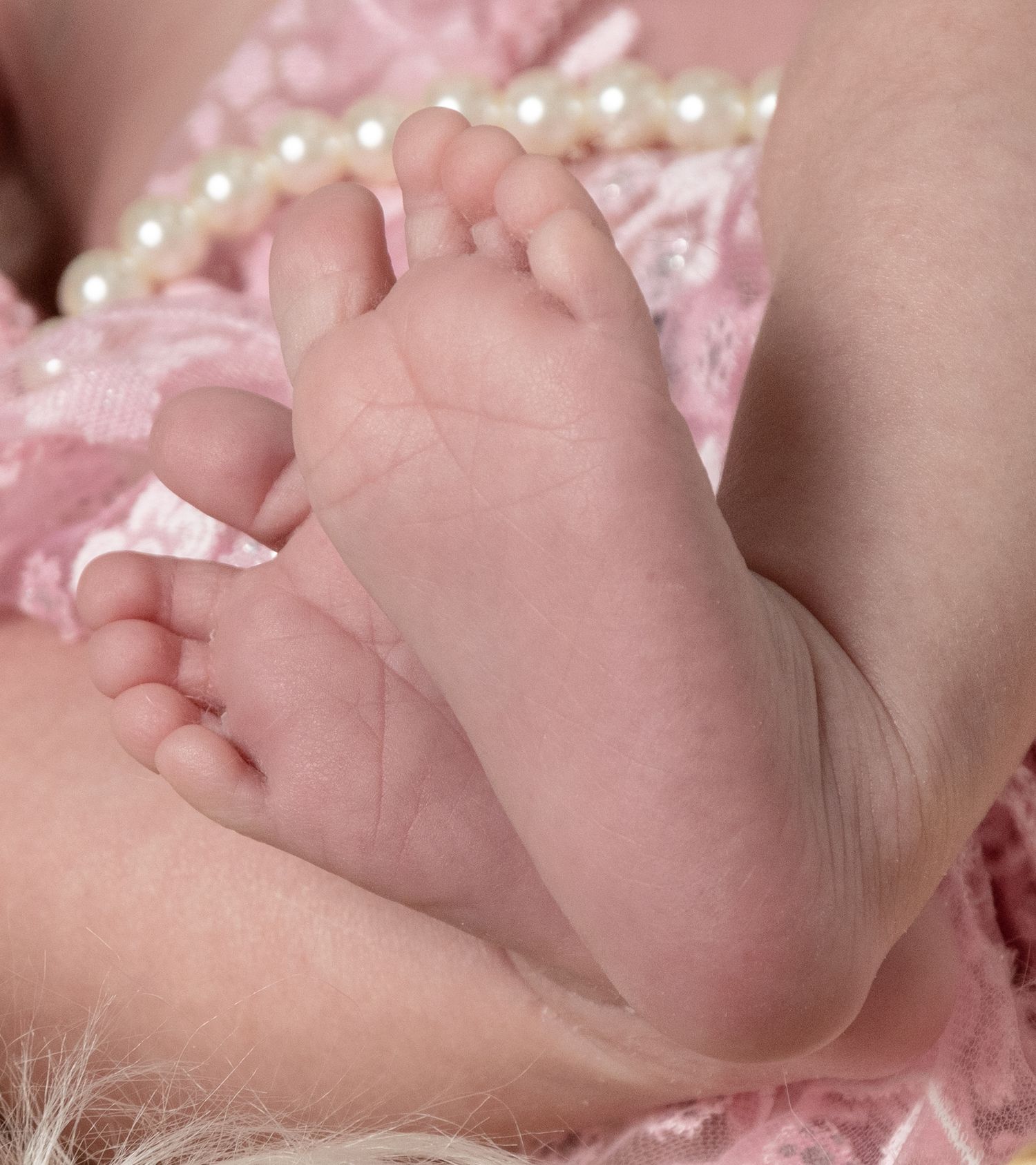 Close-up of tiny baby feet with delicate pink lace and pearl details.