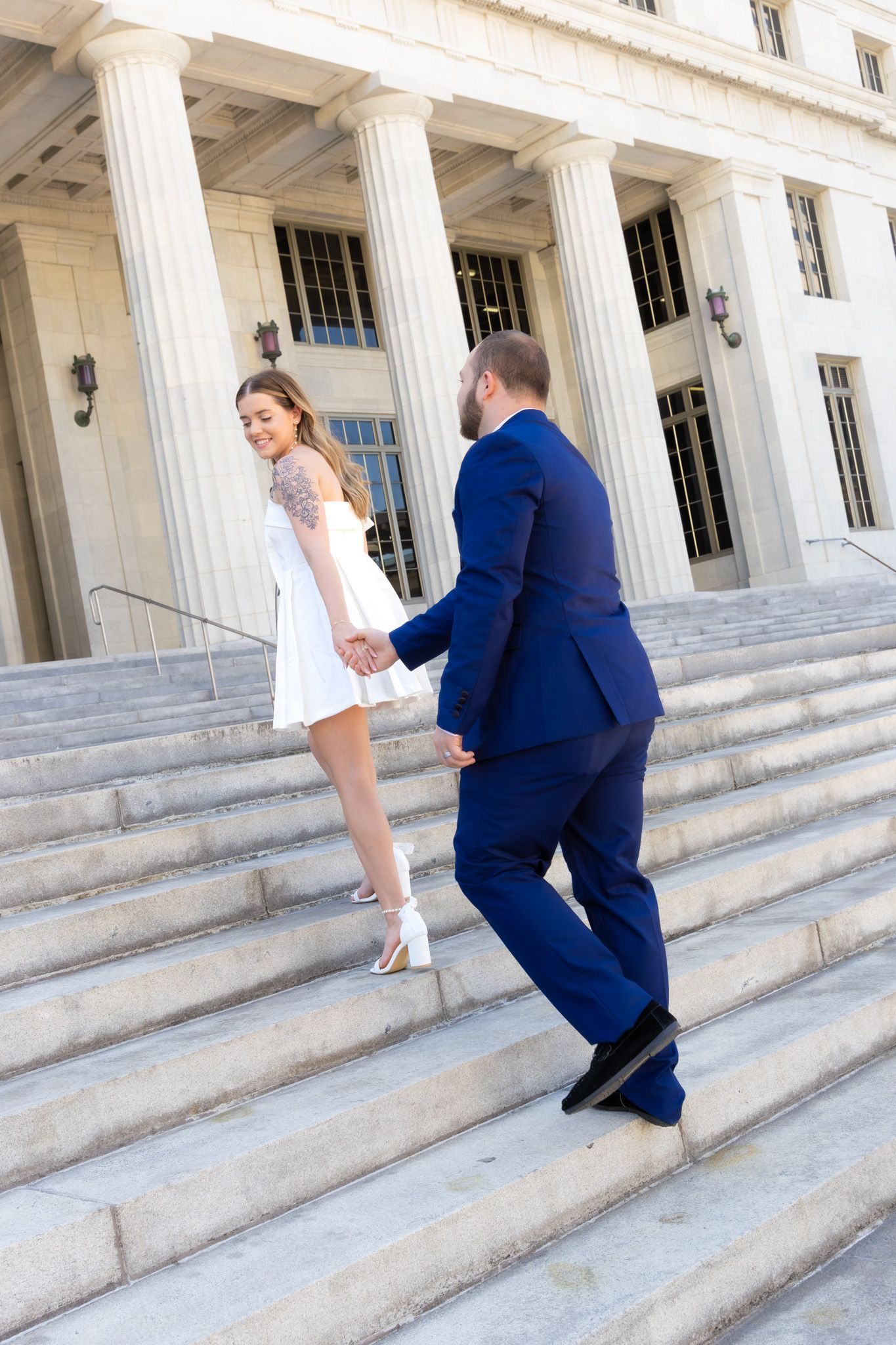 A couple ascending stone steps of a neoclassical building with white columns.