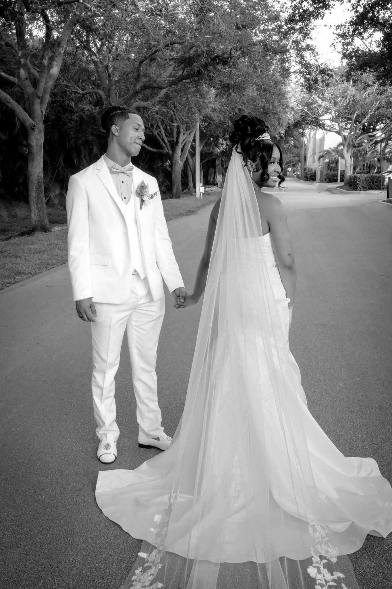 A wedding couple walking on a tree-lined path in black and white.