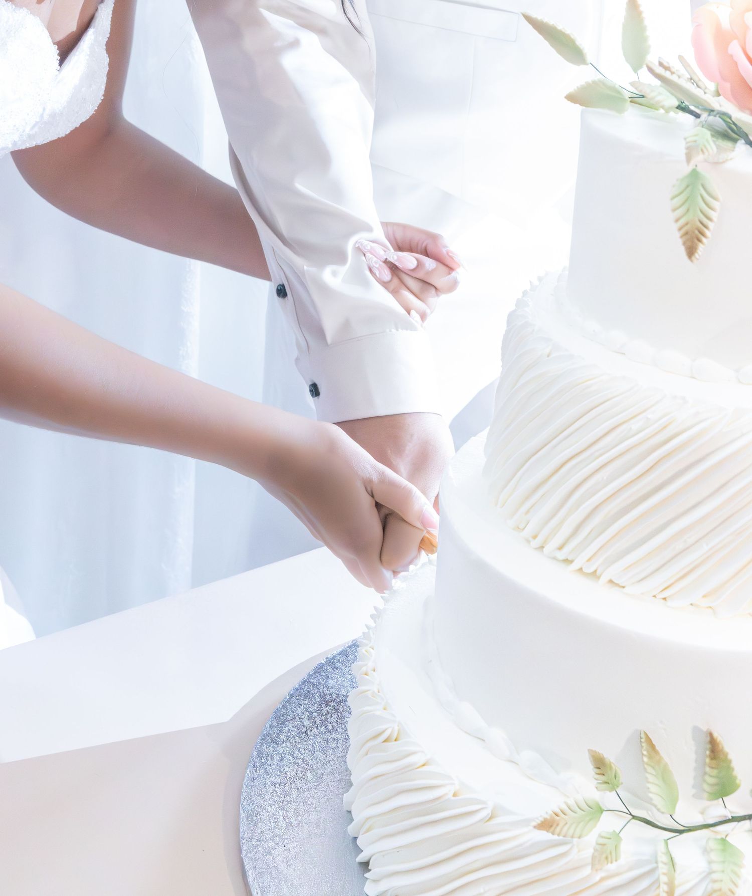 Hands cutting into an elegant white wedding cake with delicate floral details.