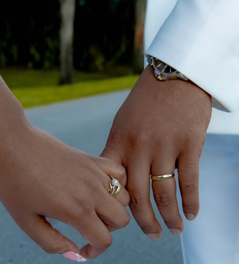 Wedding rings displayed on hands against white formal attire.