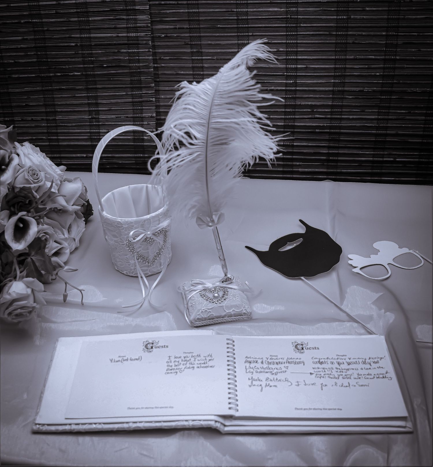 Wedding guest book with white feather pen and decorative masks on elegant table setting.